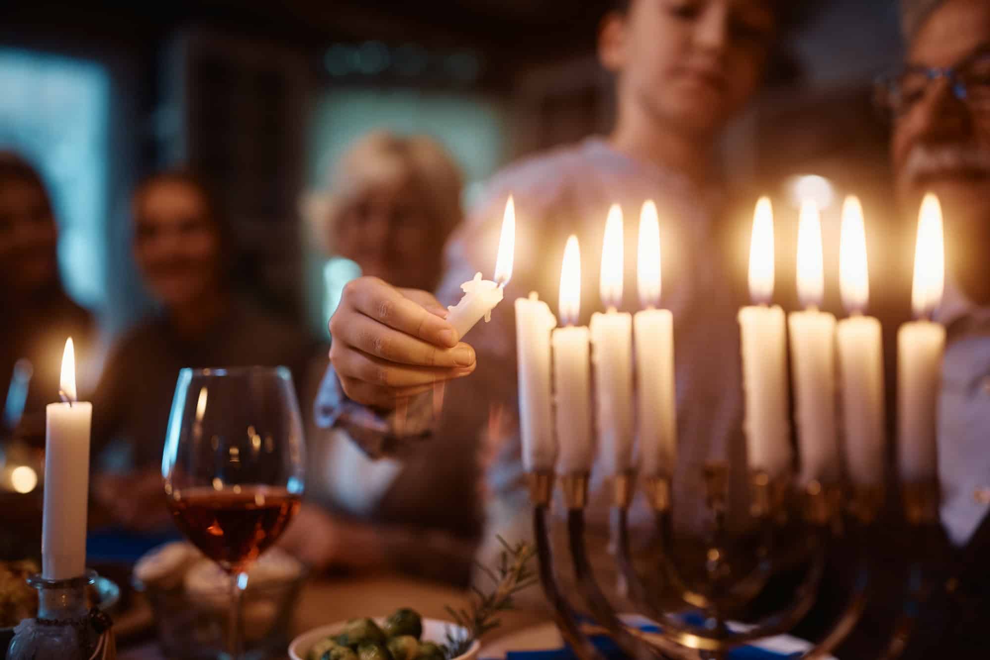 Close up of Jewish kid lighting the menorah during family dinner on Hanukkah.