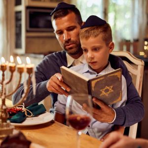 Jewish father and son reading Tanakh at dining table on Hanukkah.